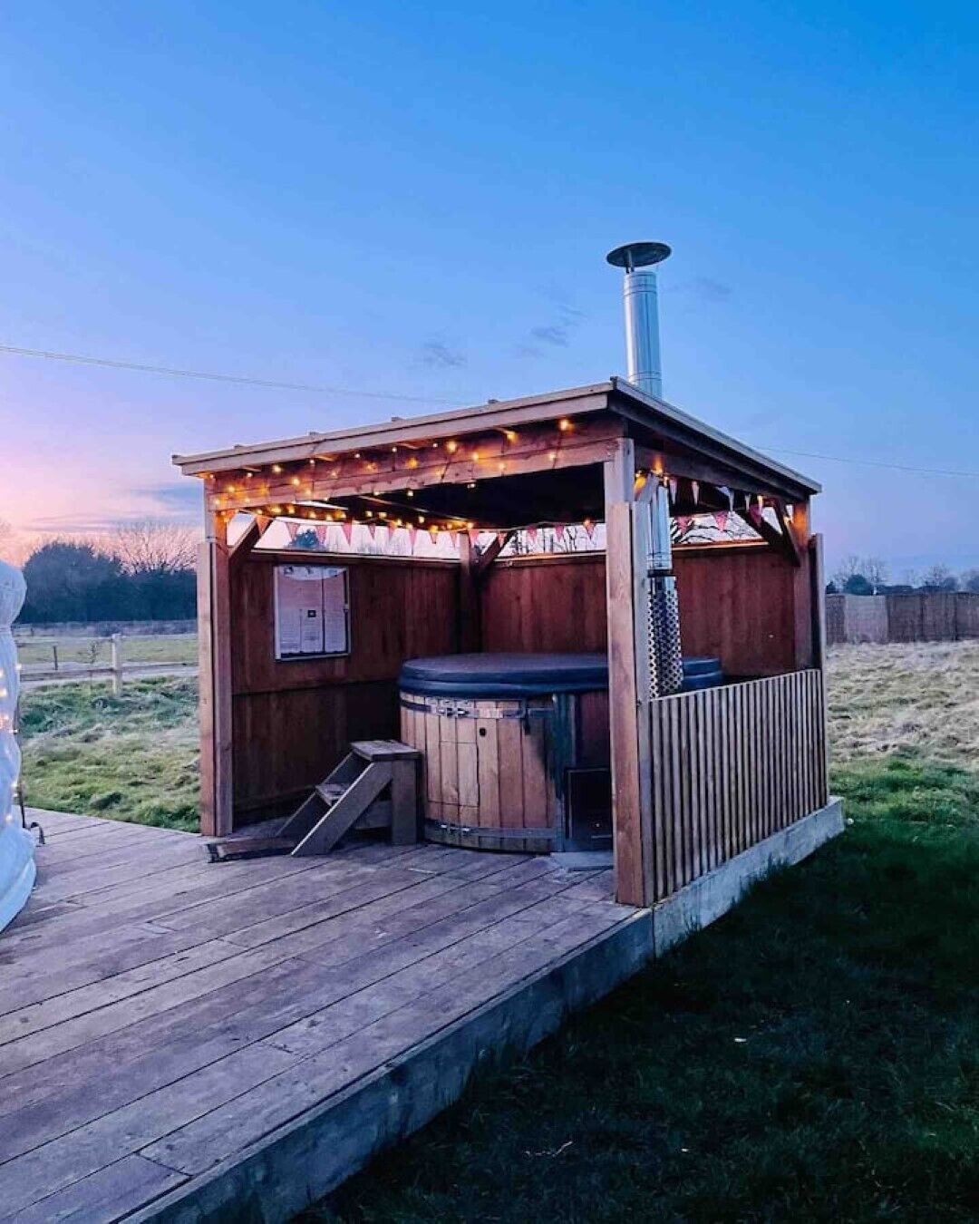 Puurakenteinen ulkotila, jossa on poreallas, savupiippu ja koristevalot.