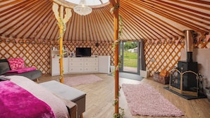 Ein Jurteninneres mit Holzboden, einem Fernseher, einem Kamin und einer gemütlichen Sitzecke.