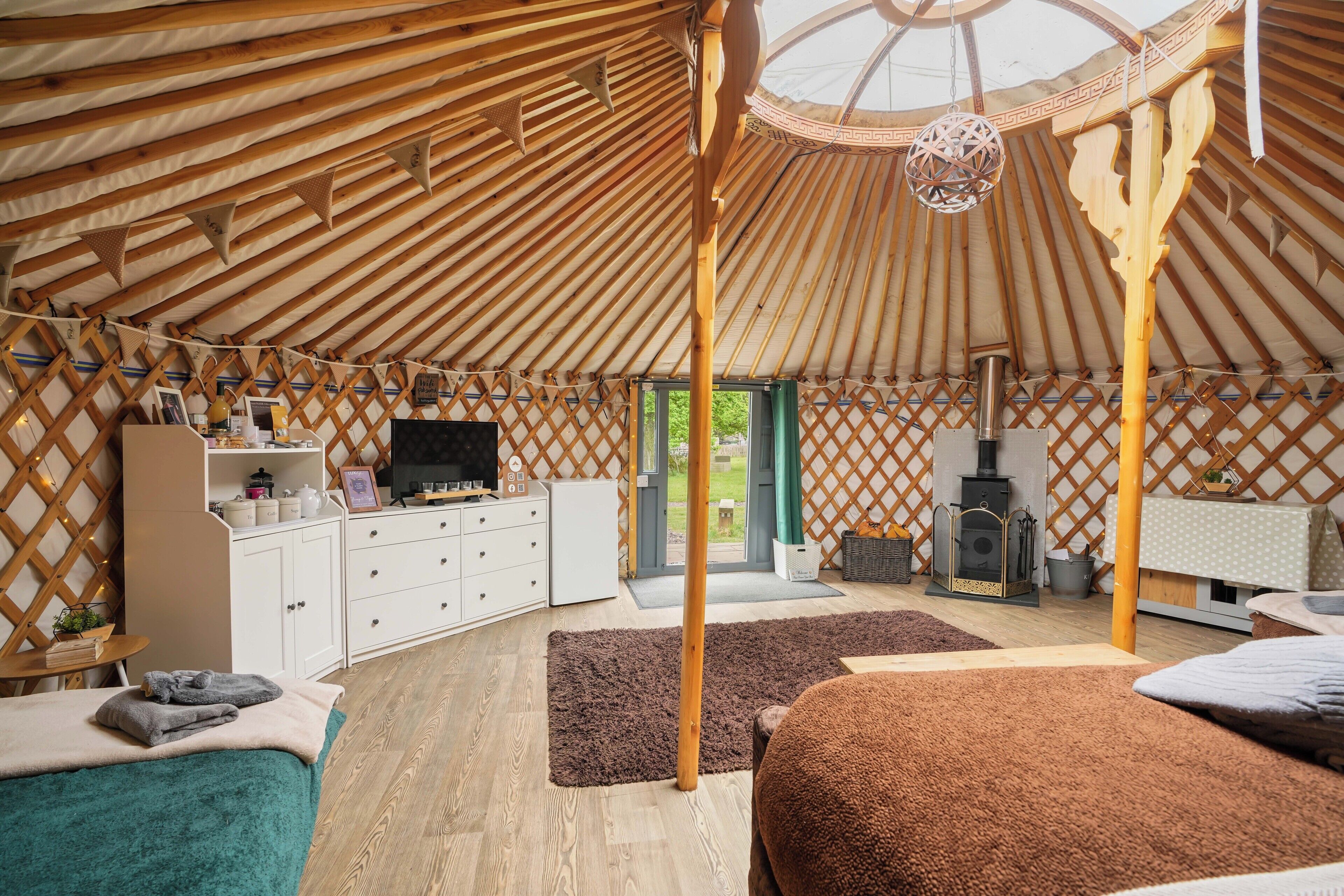 Interior de una yurta con techo de madera, un poste de madera central, un televisor, una chimenea y una zona de estar acogedora.
