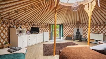 Interior de una yurta con techo de madera, un poste de madera central, un televisor, una chimenea y una zona de estar acogedora.