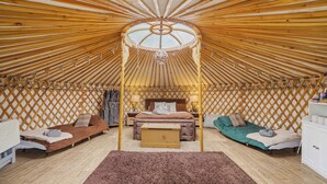 Ein Jurteninneres mit einem zentralen Bett, zwei kleineren Betten, einer Holzbalkendecke und einer Gitterwand.