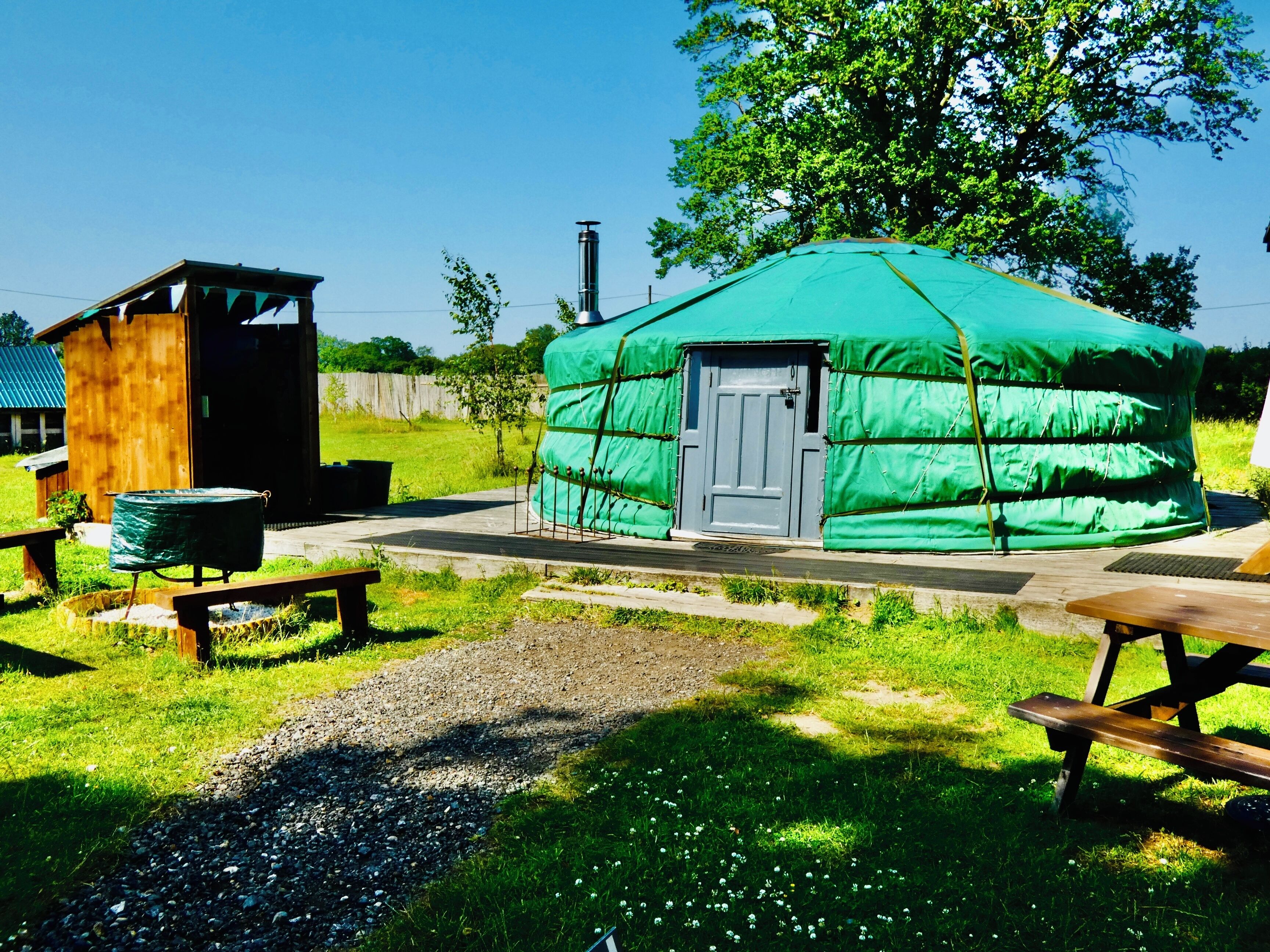 A yurt with a door, a wooden structure, and picnic tables.