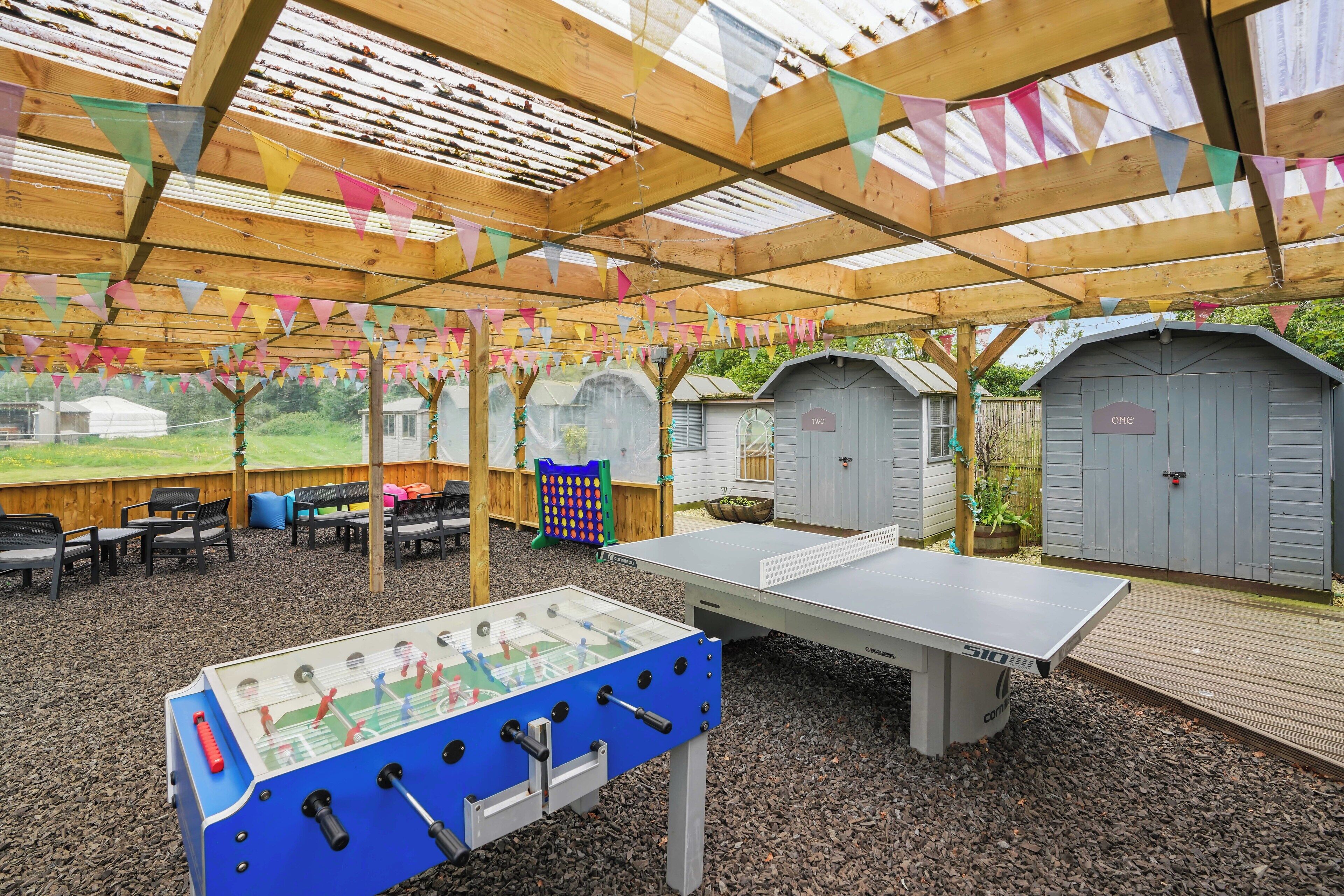 Een overdekte recreatieruimte met een tafelvoetbaltafel, een pingpongtafel en een zithoek.