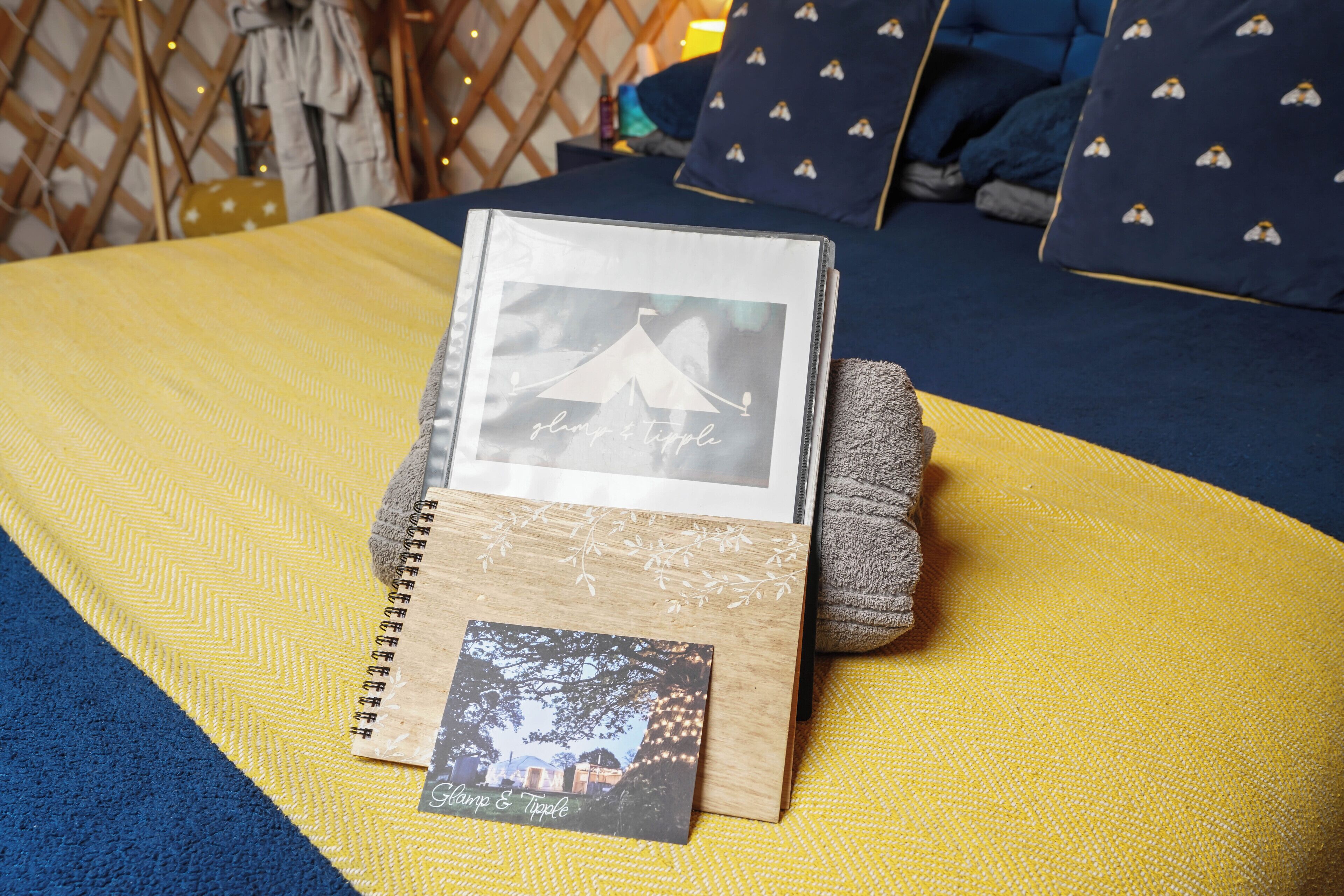 Ein Bett mit einer gelb-blauen Tagesdecke, ein Holzfotorahmen und ein kleines Notizbuch mit einem Bild und Text.
