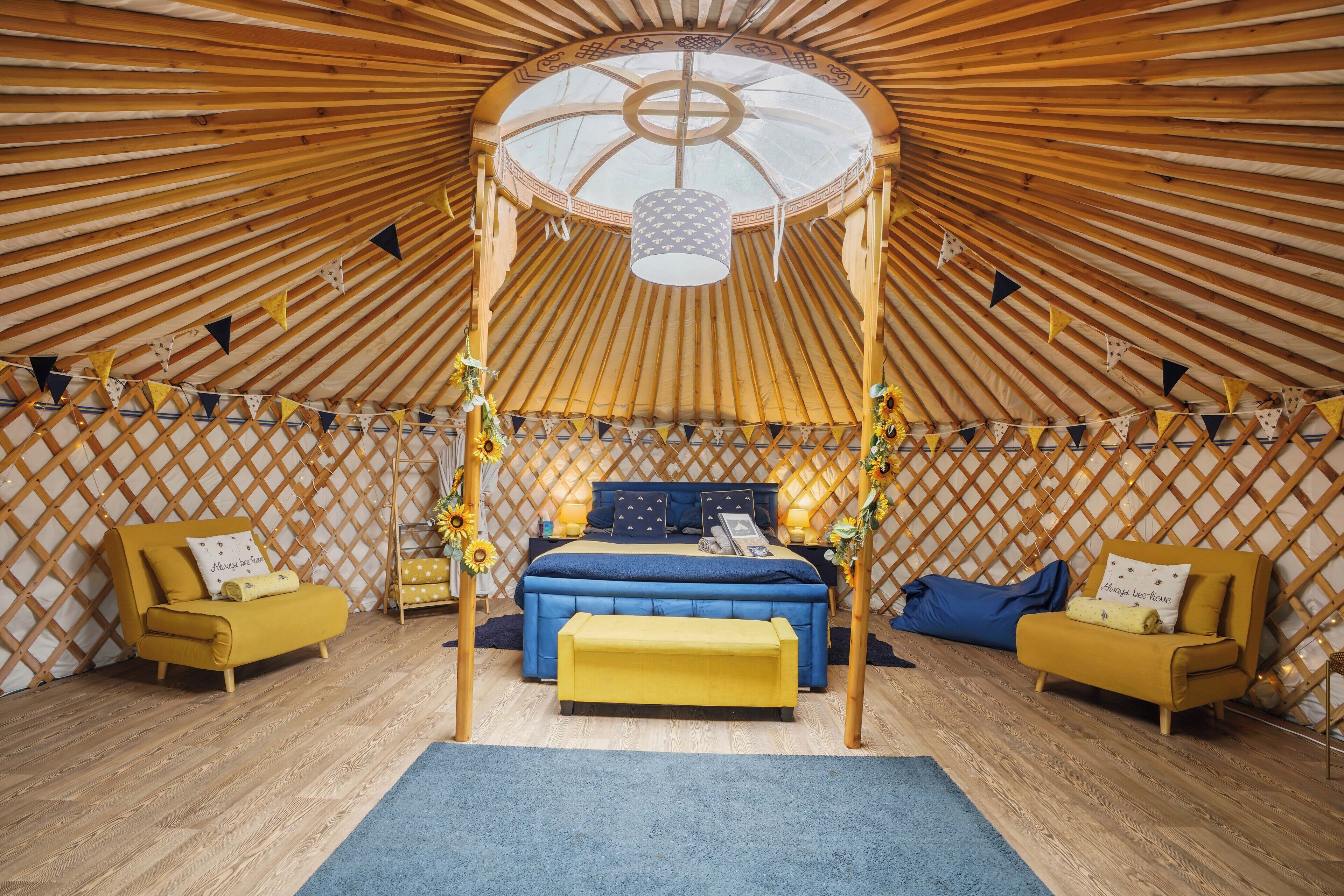 Eine Jurte mit einem zentralen Bett, zwei Sofas, einem Baldachin und einer Gitterwand.