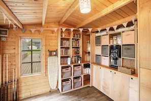 Ein Holzblockhaus-Interieur mit Holzboden, einem Fenster, einem Bücherregal, Aufbewahrungsbehältern und einer Küchenzeile.