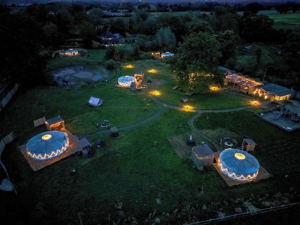 An aerial view of a rural property with several yurts and a large central building, surrounded by trees and open fields.