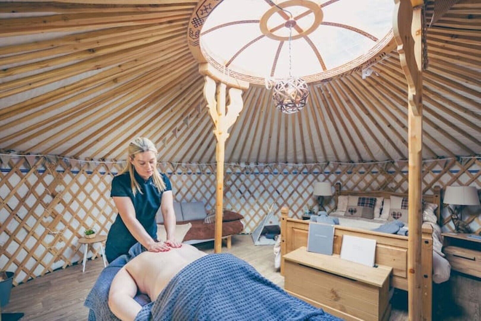 A yurt with a wooden interior, a massage table, and a person attending to a client.
