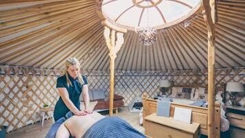 A yurt with a wooden interior, a massage table, and a person attending to a client.