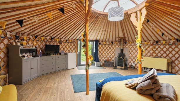 A yurt interior with a bed, wooden furniture, a television, and a fireplace.