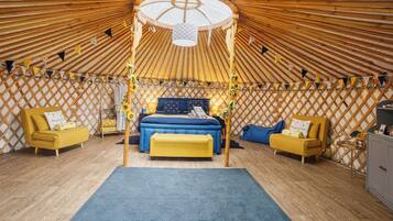 Ein gemütlicher, runder Raum mit einem Bett unter einem Baldachin, umgeben von gelb-blauer Einrichtung und einer Holzwandverkleidung.