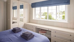 Un dormitorio con cama, escritorio, silla, armario y ventana con vista a edificios y árboles.