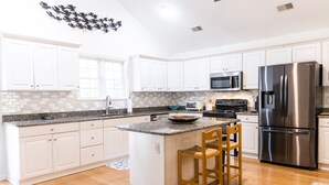 A modern kitchen with white cabinets, a stainless steel refrigerator, a microwave, and a granite countertop. - Exceptional 4 bedroom coastal cottage with heated pool access, walk to the beach (Edisto Island)