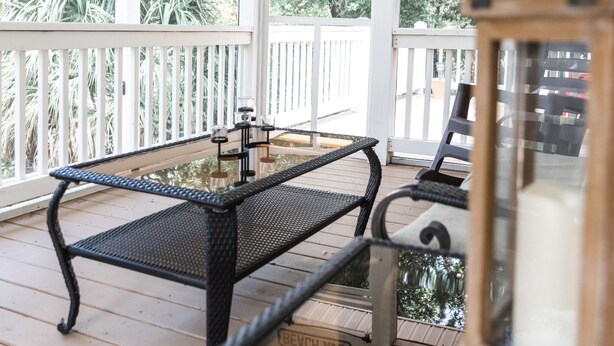 A covered porch with a table and chairs, a street sign reading "BEACH AVE", and a view of trees. - Exceptional 4 bedroom coastal cottage with heated pool access, walk to the beach (Edisto Island)