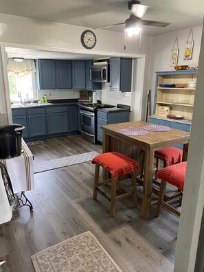 A kitchen with blue cabinets, a microwave, and a stove. There is a wooden table with red stools and a clock on the wall.