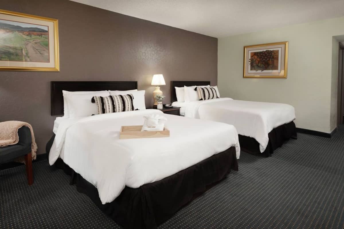 A hotel room with two beds, a nightstand, a lamp, and a framed picture on the wall.