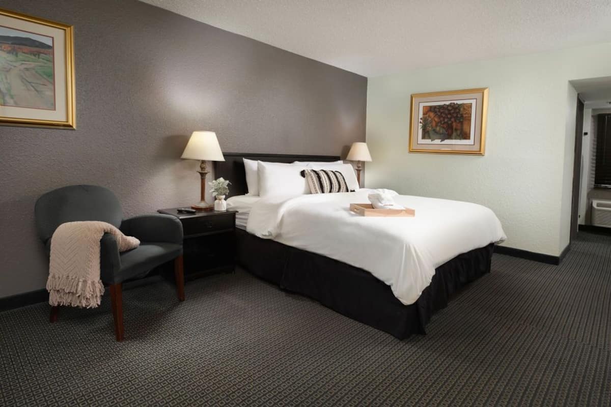 A hotel room with a bed, two bedside tables, a chair, a lamp, and artwork on the walls.
