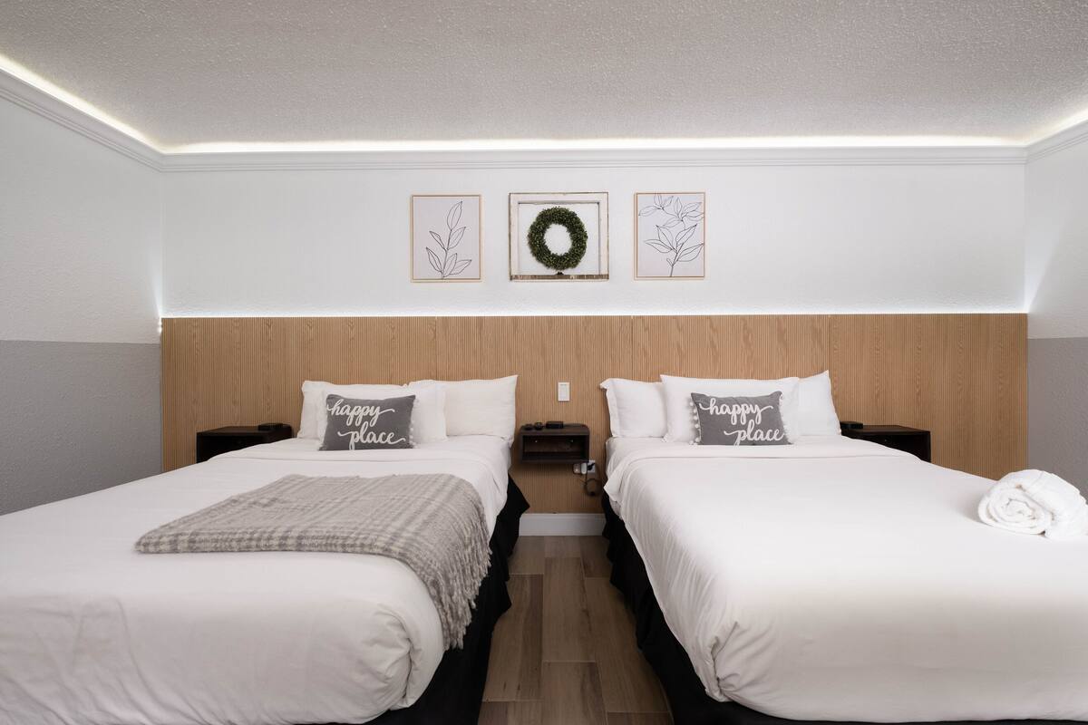 A hotel room with two beds, a wooden headboard, a wall-mounted wreath, and framed botanical prints.