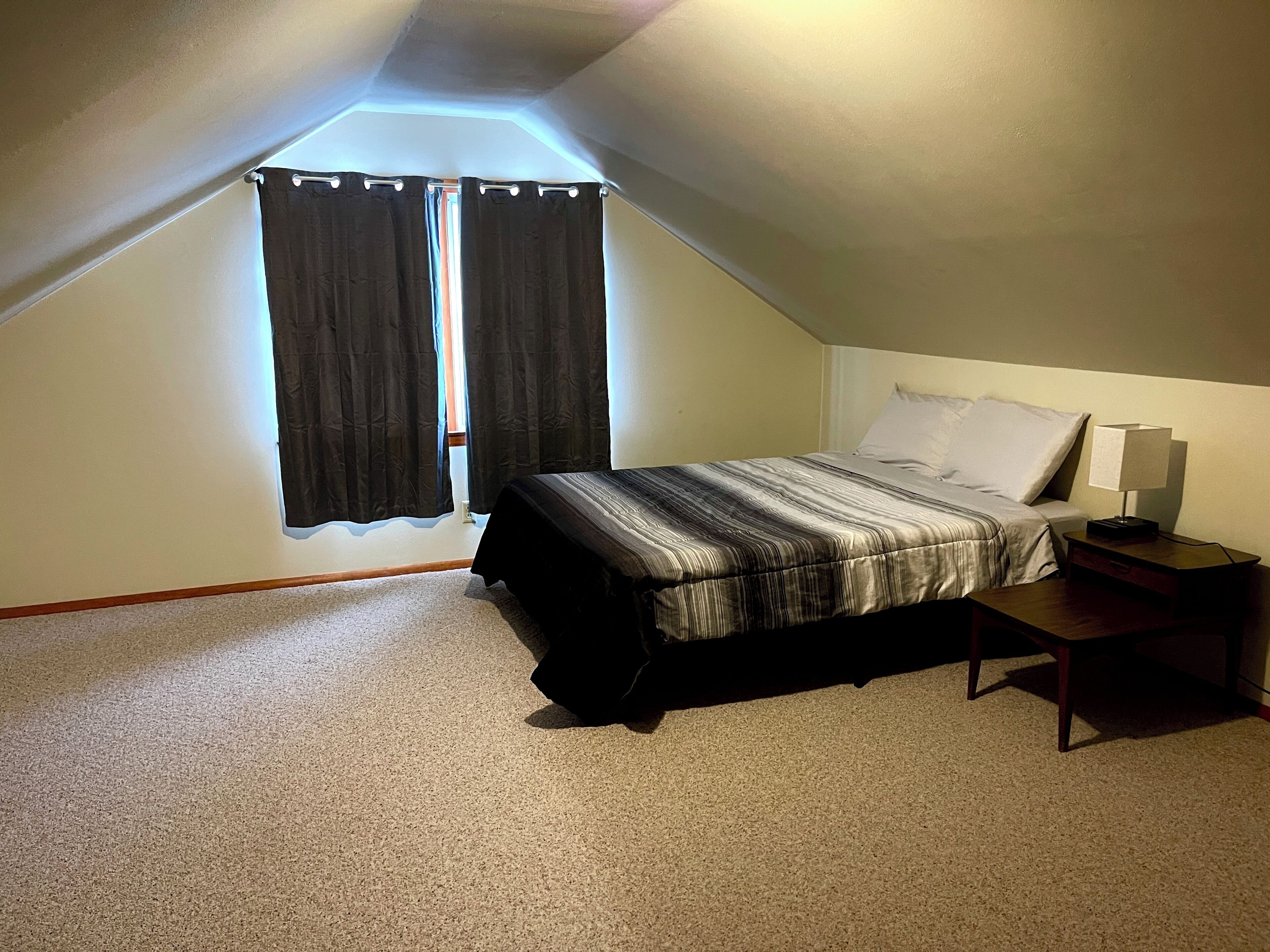 A bedroom with a bed, a nightstand, and a window with curtains.