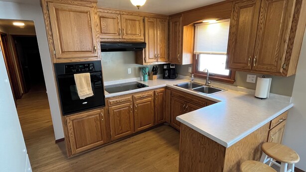 A kitchen with wooden cabinets, a black oven, a sink, and a window with blinds.