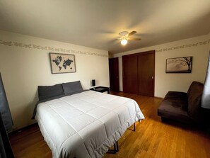 A bedroom with a bed, a nightstand, a chair, a wardrobe, and a ceiling fan.