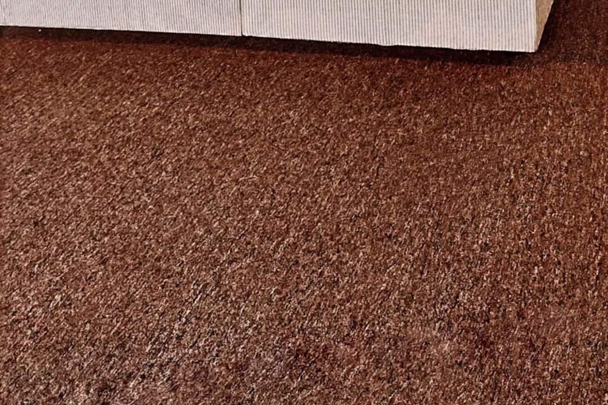 A bed with a wooden headboard, white bedding, and a brown carpet.