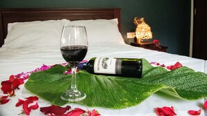 Una cama con una botella de vino y una copa, una mesita de noche con una lámpara, y una pared verde.