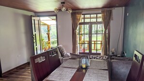 Un comedor con mesa y bancos de madera, ventilador de techo y vistas al exterior con vegetación.