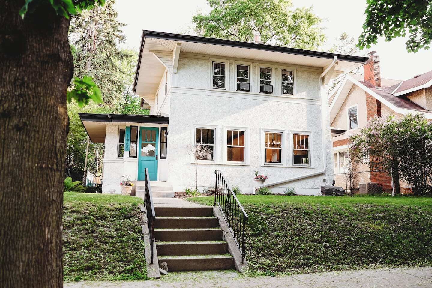 Une maison à deux étages avec un porche à l’avant, une porte bleue et un escalier menant à l’entrée.