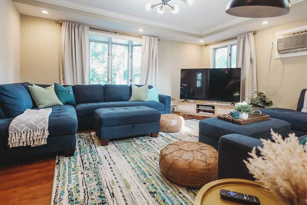 A living room with a sectional sofa, ottoman, TV, and a coffee table with decorative items.