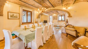 A dining area with a long table set for a meal, surrounded by white chairs, a sofa, and a wooden floor. - Pool Villa Angela With Sauna, Jacuzzi and Gym (Manciano)