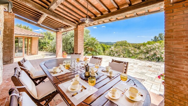 An outdoor patio with a wooden table set for dining, surrounded by chairs, and a view of greenery and hills. - Pool Villa Angela With Sauna, Jacuzzi and Gym (Manciano)