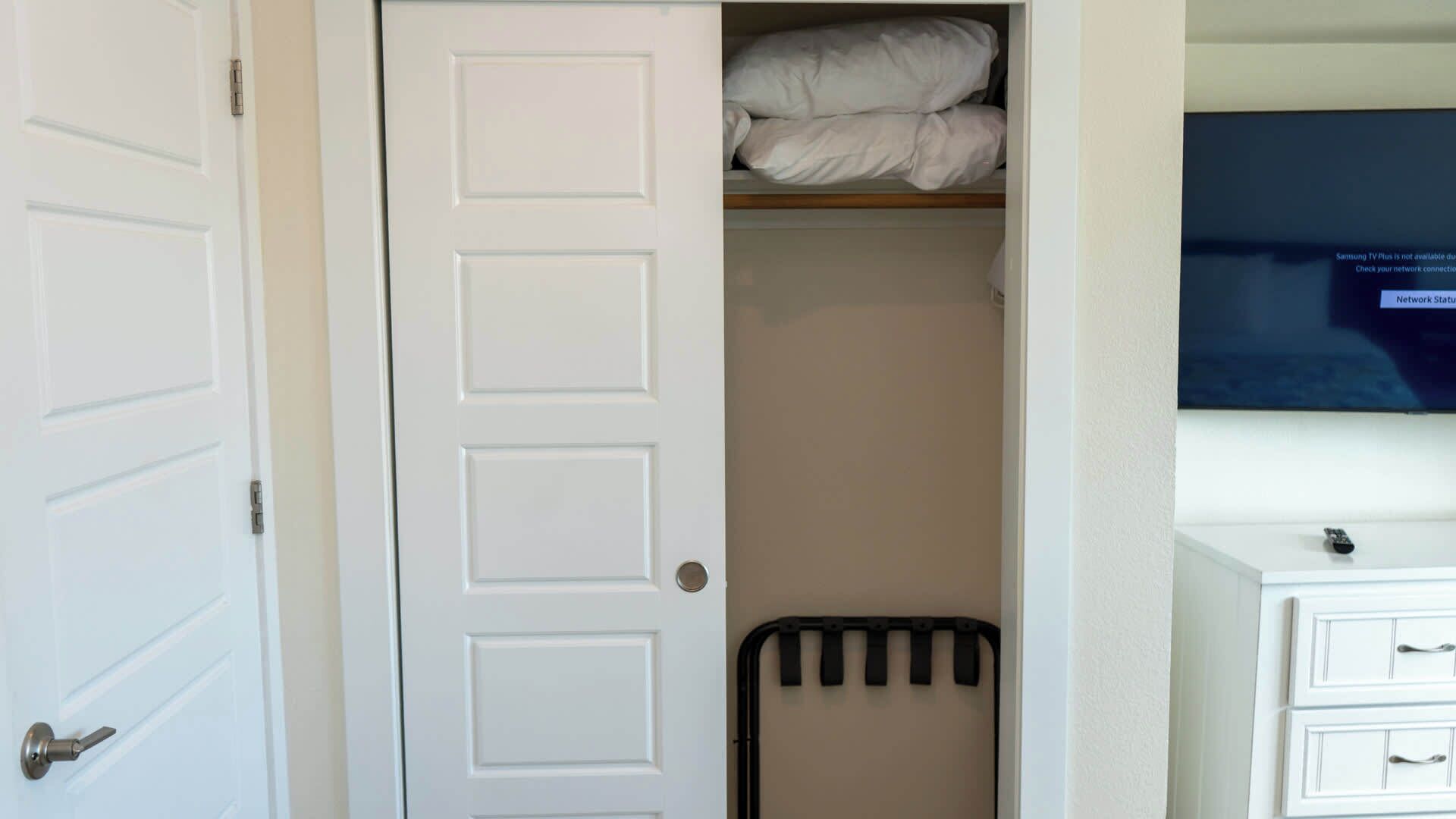 A room with a white door, a bed with white bedding, a radiator, a television on the wall, and a small cabinet with drawers.