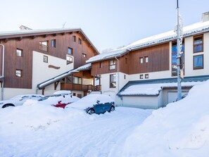 En bygning med flere vinduer og altaner, omgivet af snedækket jord og parkerede biler.