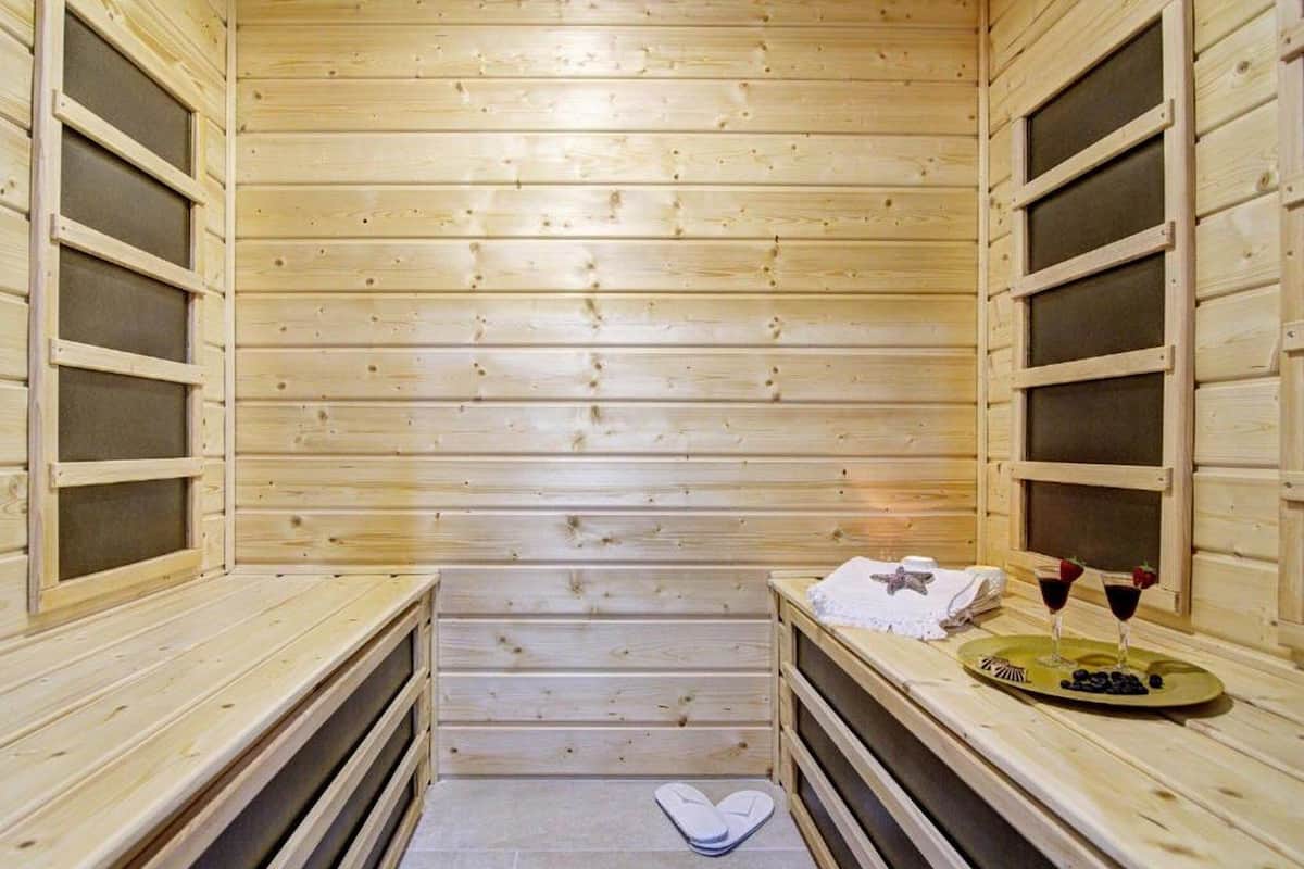 Una sauna con paredes y bancos de madera, una toalla y dos copas de vino sobre el banco.