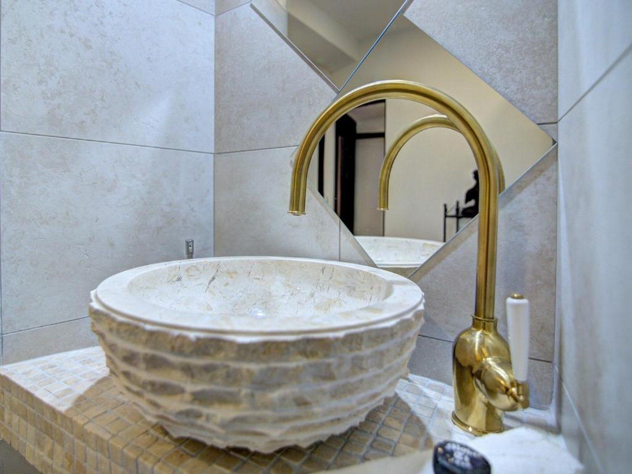A bathroom with a stone sink, gold faucet, and a mirror reflecting the room.
