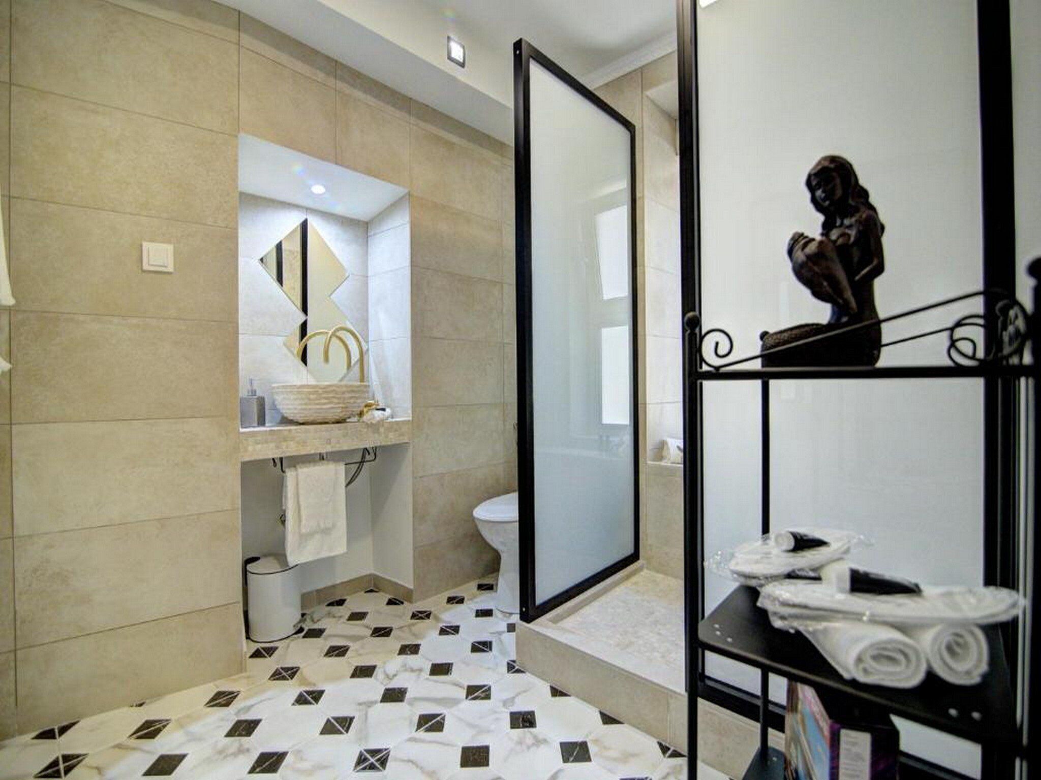 Uma casa de banho moderna com um espelho grande, uma sanita, uma zona de duche e lavatório com uma bacia decorativa.