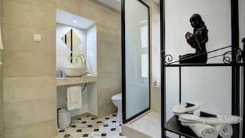 Uma casa de banho moderna com um espelho grande, uma sanita, uma zona de duche e lavatório com uma bacia decorativa.
