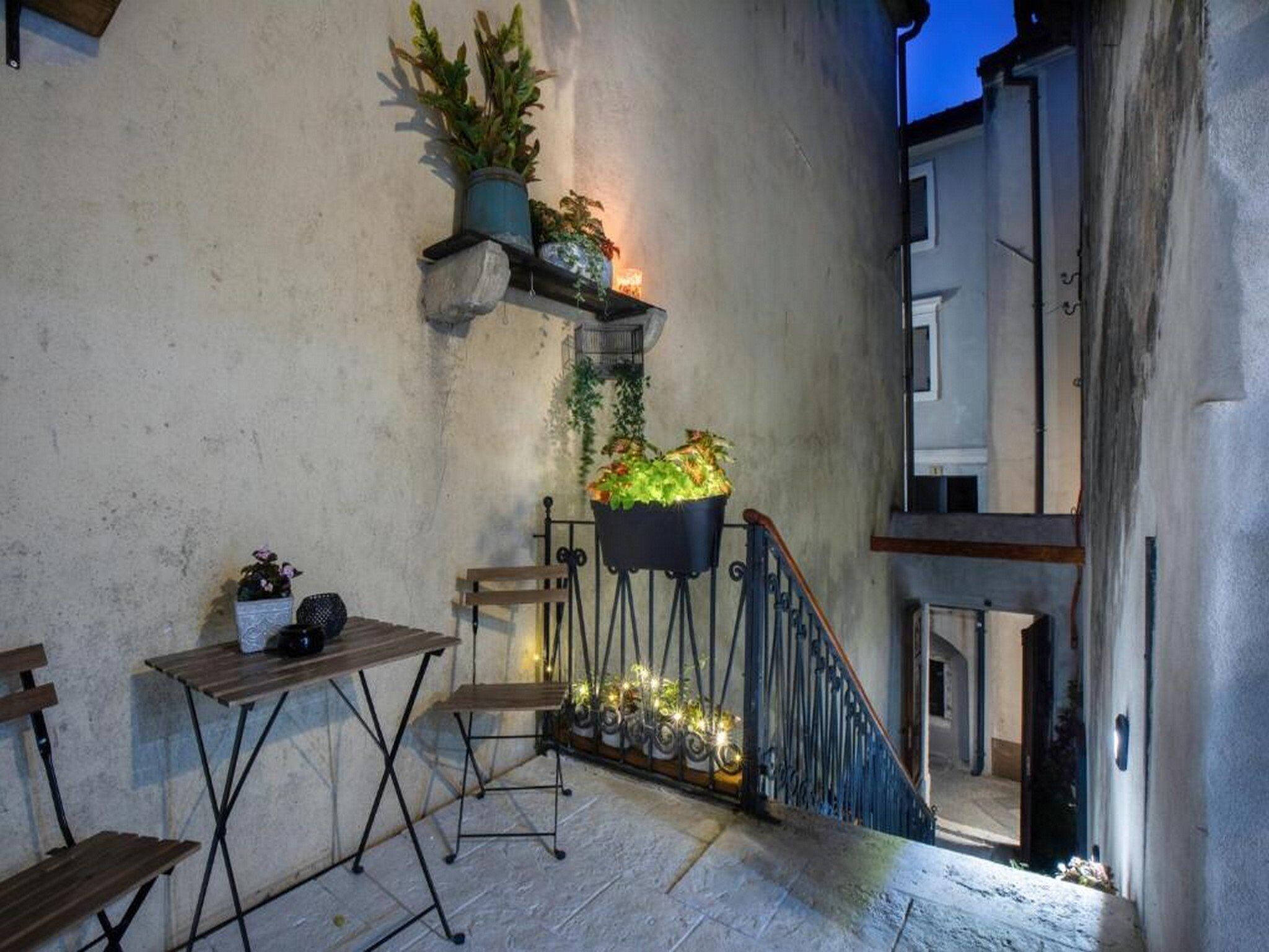 A small outdoor seating area with a table and chairs, a staircase, and potted plants against a wall.