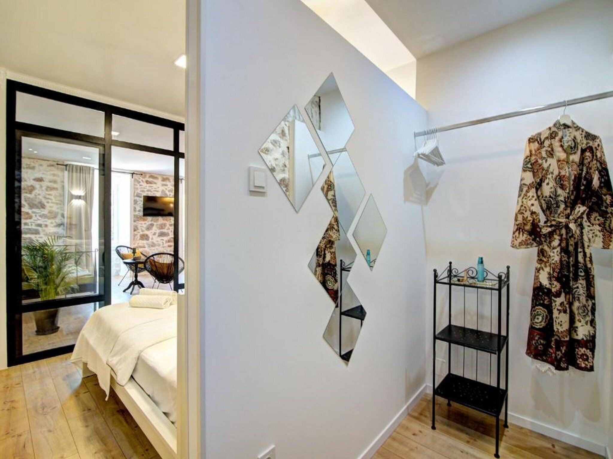 A modern bedroom with a bed, a wooden floor, and a view of a stone wall and balcony.