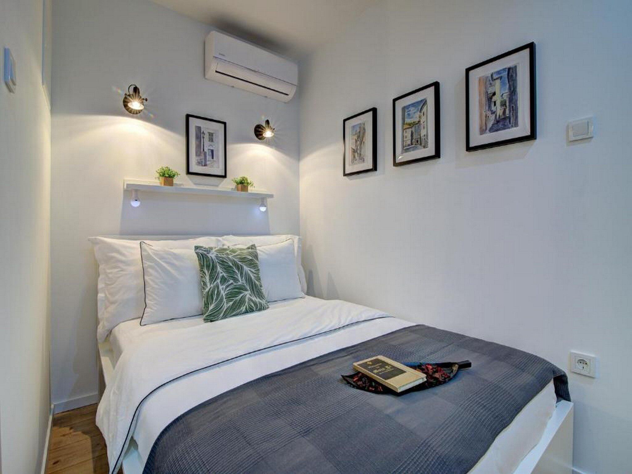 A bedroom with a bed, a bedside table, an air conditioner, and wall-mounted lights.