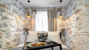 Una habitación acogedora con paredes de piedra, una cama con cabecera floral y una bandeja con cruasanes y una taza.