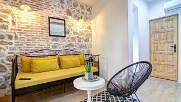 A room with a stone wall, a yellow sofa, a round white table, and a black chair.