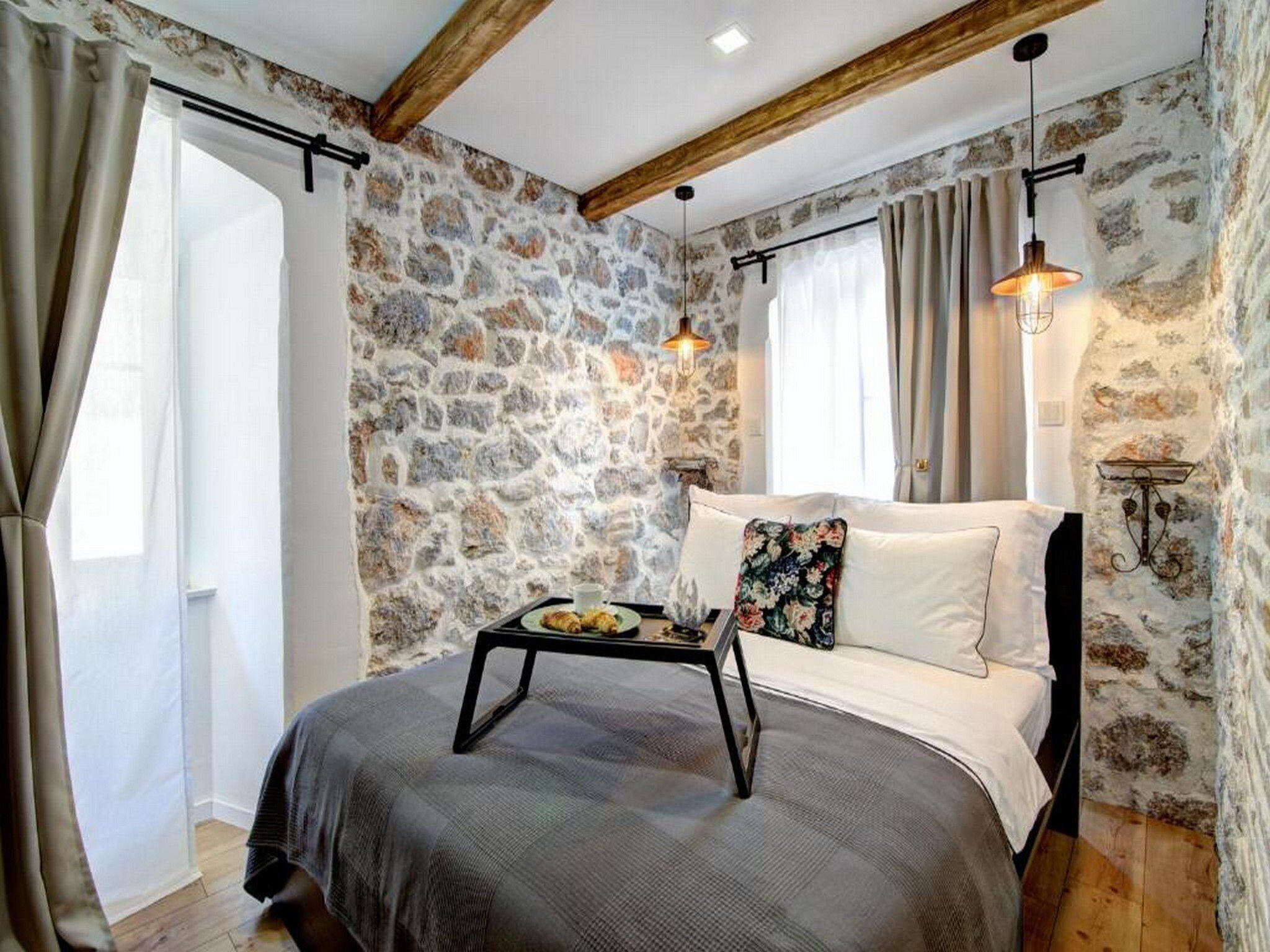 Ein Schlafzimmer mit Steinwand, einem Bett mit Blumenkissen, einem Nachttisch mit Tablett und zwei Pendelleuchten.