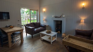 A cozy living room with a fireplace, a television, and a dining area with a table and chairs. - Remote & awe-inspiring Sealgair Cottage. Pet-friendly, log burner, lochside. (Shieldaig)