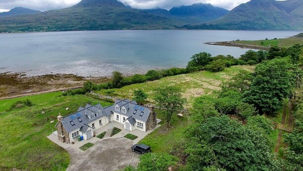 A large, modern house with multiple rooms, a driveway, and a view of a lake and mountains. - Remote & awe-inspiring Sealgair Cottage. Pet-friendly, log burner, lochside. (Shieldaig)