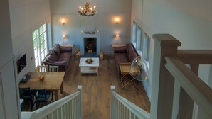A spacious loft-style living area with a fireplace, leather sofas, a dining table, and a staircase. - Remote & awe-inspiring Sealgair Cottage. Pet-friendly, log burner, lochside. (Shieldaig)