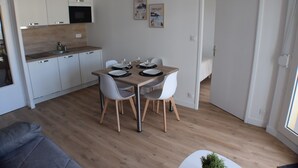 A modern kitchen with white cabinets, a wooden dining table, and chairs. There are framed pictures on the wall and a hanging light fixture. - Ideal location for beach and pink granite coast. Sea view from the balcony (Perros-Guirec)