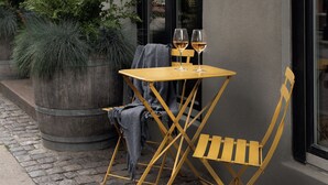 A restaurant with outdoor seating, including a table and chairs, and a large planter with plants.