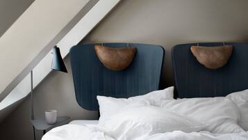 A neatly made bed with white linens, a small bedside table with a lamp, and a headboard with a unique design.